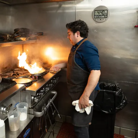 A chef working a flaming pan on the line
