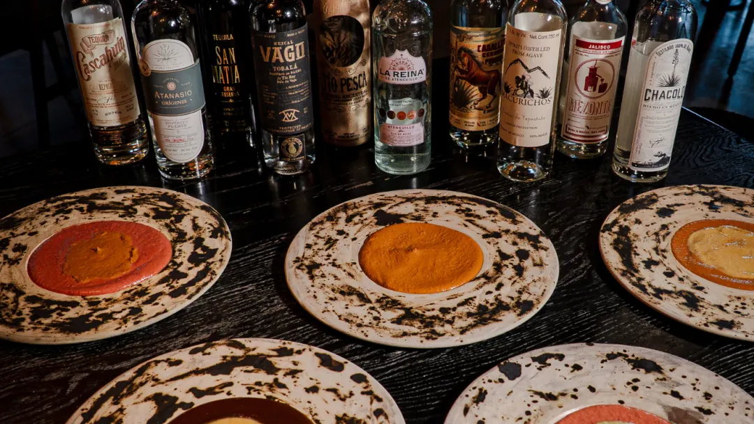 A flight of moles on hand-painted plates in front of tequila bottles